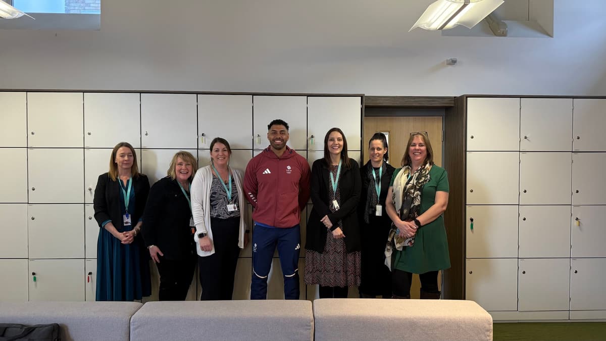 School staff members stand together smiling in a staff room after a school visit.